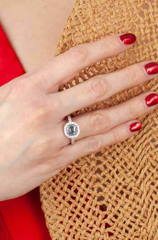 Hand wearing a ring with an Aquamarine gemstone holding a hat.