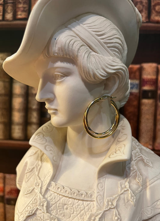 A close-up of a white classical-style bust wearing a large gold hoop earring, 