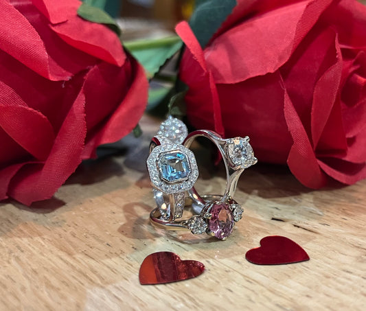 Two rings with gemstones on a wooden surface with red roses and heart-shaped objects.