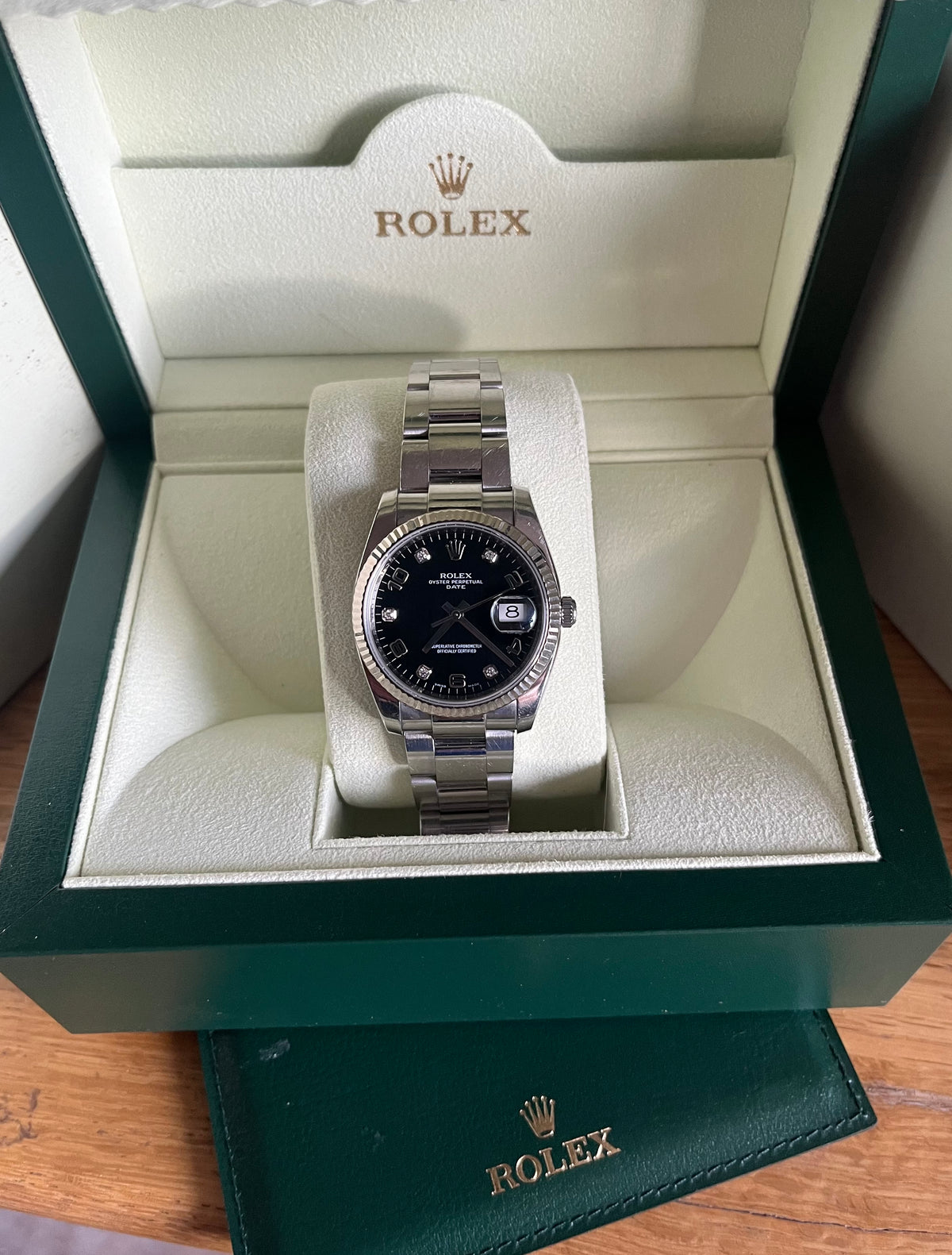A Rolex wristwatch with a stainless steel Oyster bracelet and black dial, presented inside an open green Rolex gift box on a wooden surface.